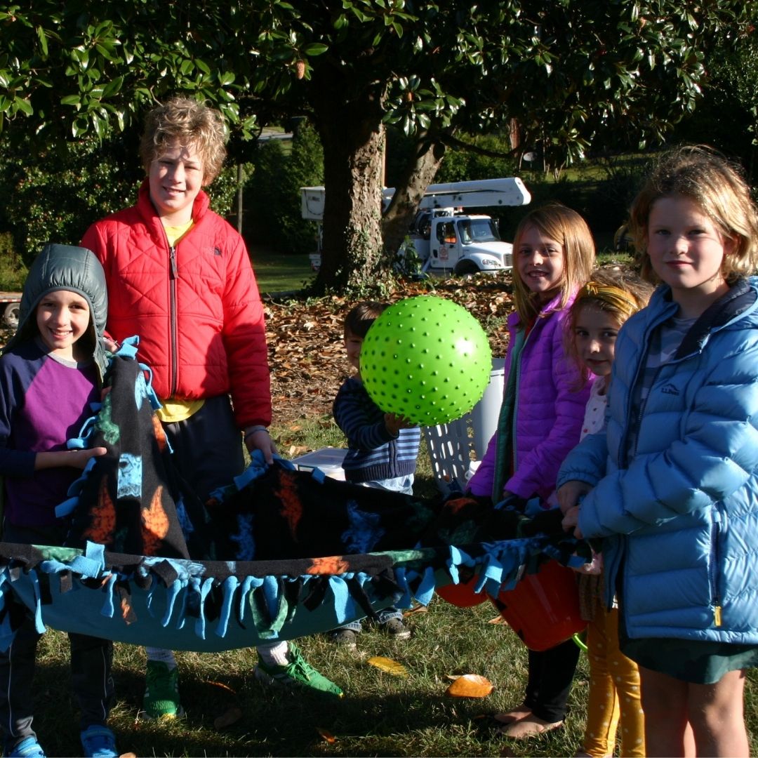 children outside lifting a blanket they made