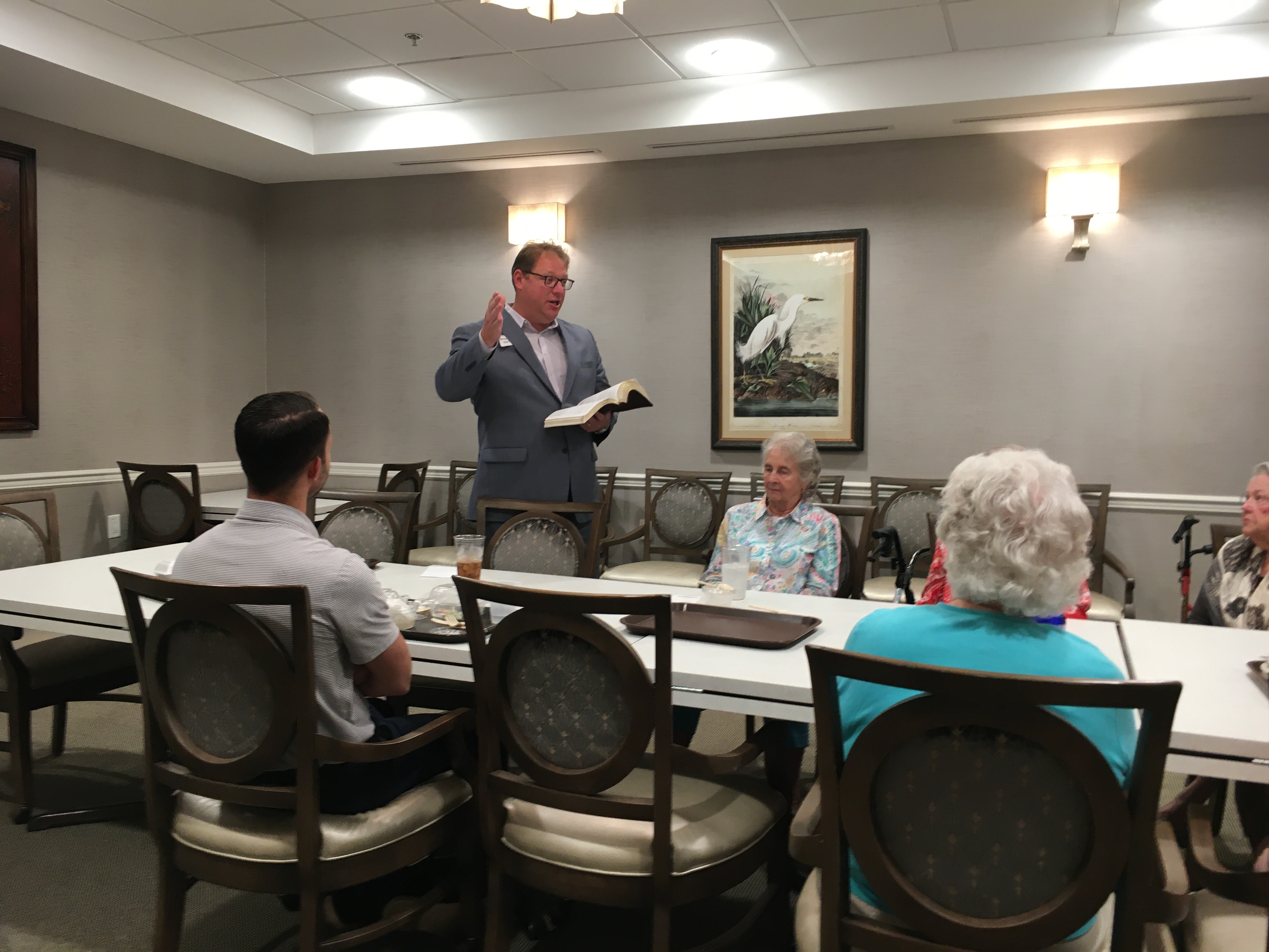 man standing with an open bible sharing with a group of older people