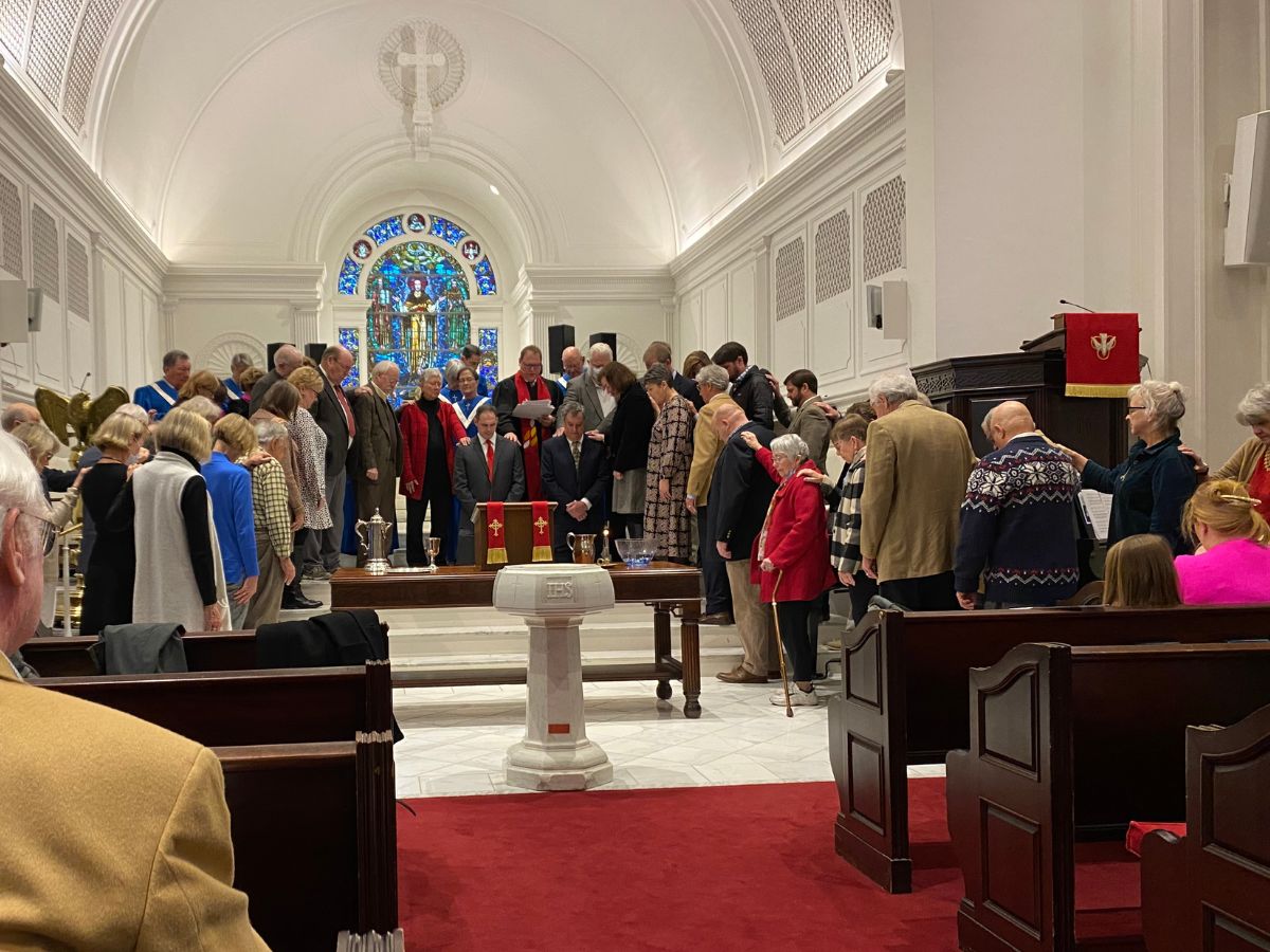 a group of people in front of a church laying their hands on two men who are kneeling as part of a Session ordination and installation service