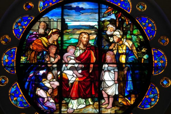 stained glass window image of Jesus welcoming children and sitting on his lap
